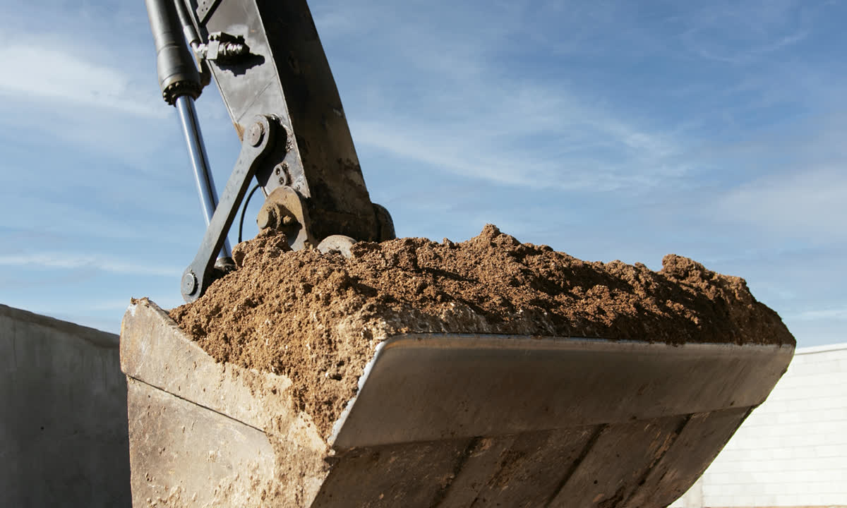 Excavator arm and bucket working above prepared earth